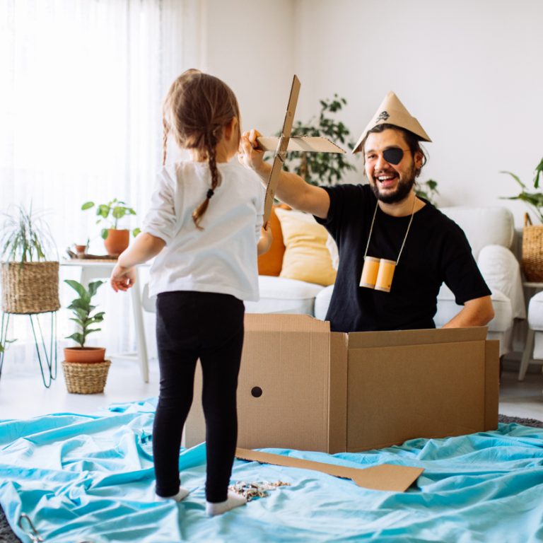 Playful childhood. Little girl and young father having fun with cardboard box. Daughter and father pretending to be on ship