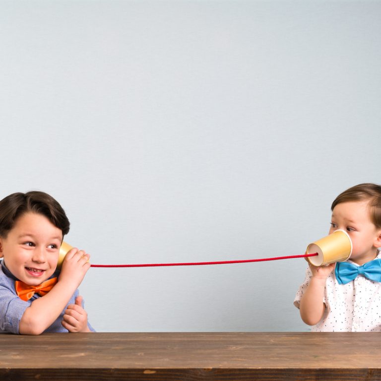 Two childeren are using paper cups as a telephone